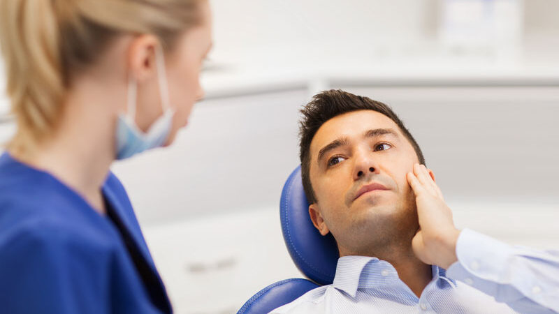 Image of a new patient holding the side of his jaw as he talks to a dental assistant about having a root canal.